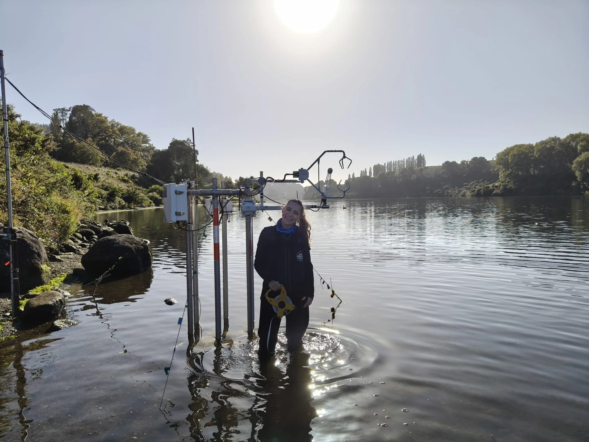 Photo: A woman is standing knee-deep in water in front of a measuring device, holding a tape measure.